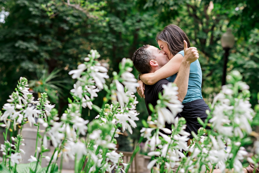 A man gives a thumbs up as his lifts his fiance up in his arms for a kiss.
